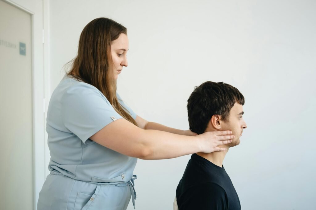 A physiotherapist performs a neck adjustment on a male patient in a clinic setting.