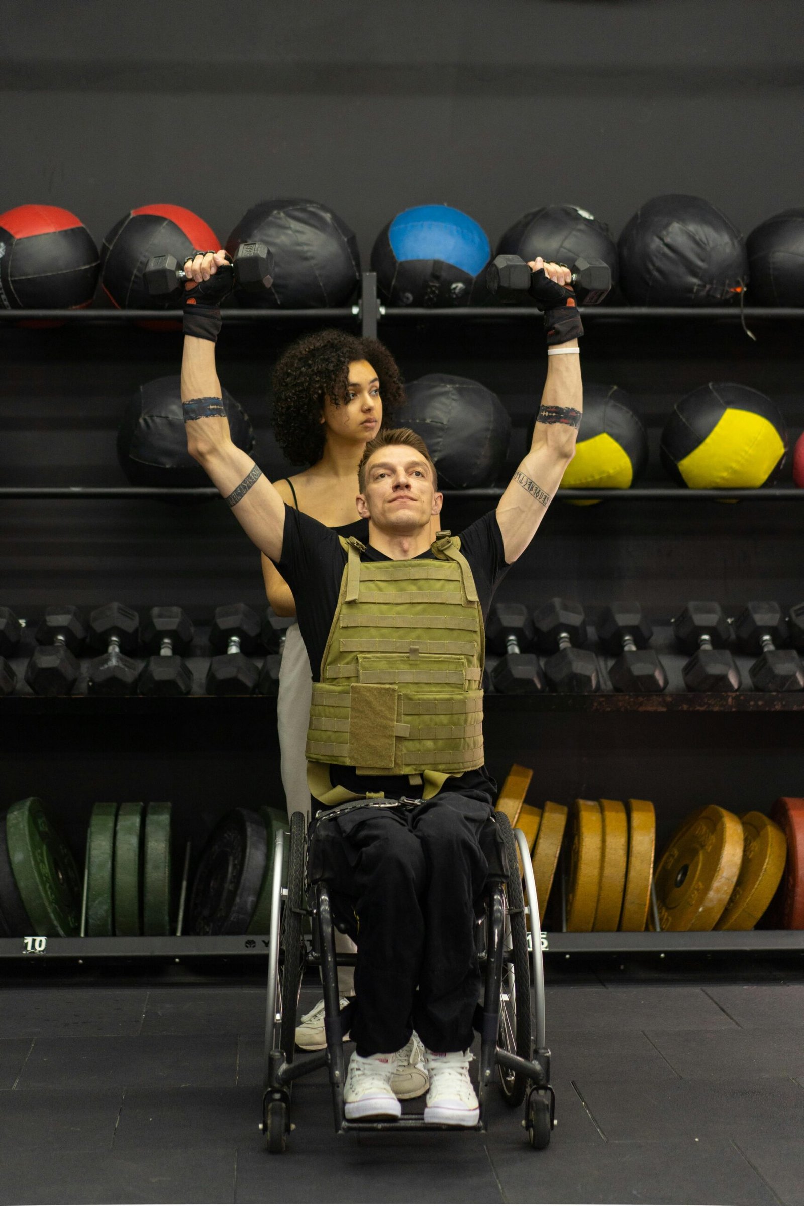 A man in a wheelchair performs strength training with a trainer's support, with physiotherapy (sports physiotherapy)
